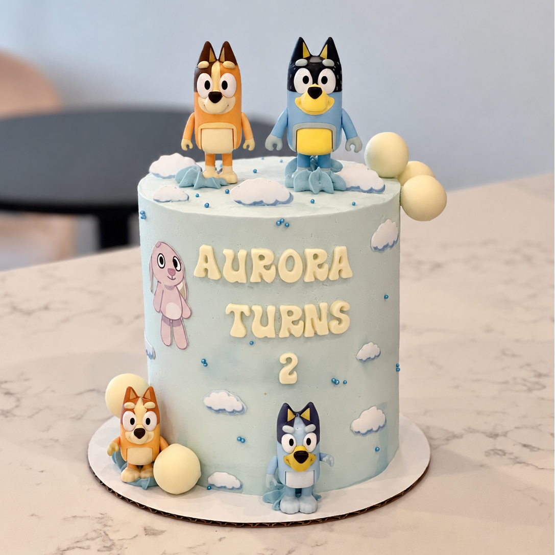 pale blue cake with cartoon dog figures, cloud details, cream spheres and a piped birthday message