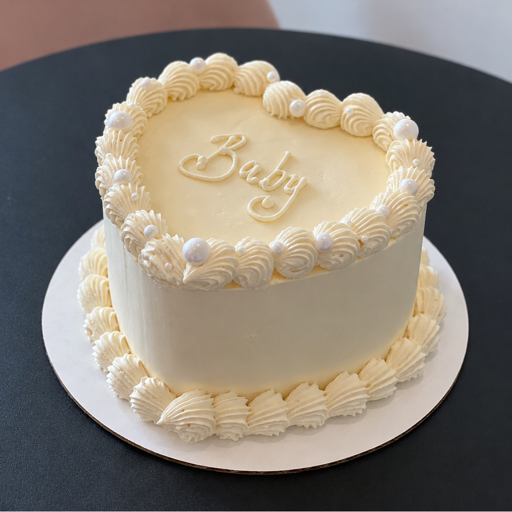 white heart-shaped cake with piped borders and 'baby' written on top