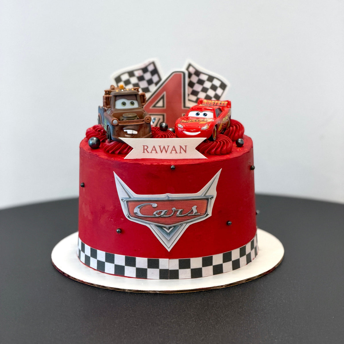 red cake with racing car figures, checkered flags, a number 4 and a name banner