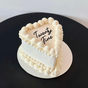 heart-shaped white cake with piped borders and a black piped message