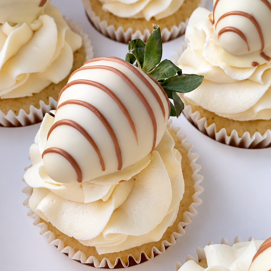 cupcakes with cream frosting, one topped with a striped dipped strawberry